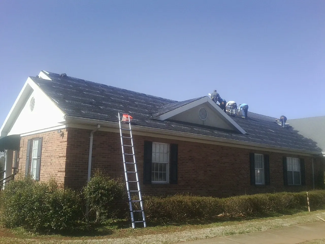 Crew tearing shingles off a brick ranch roof with a ladder set — Metal Roof Repair work by our crew in Fort Deposit