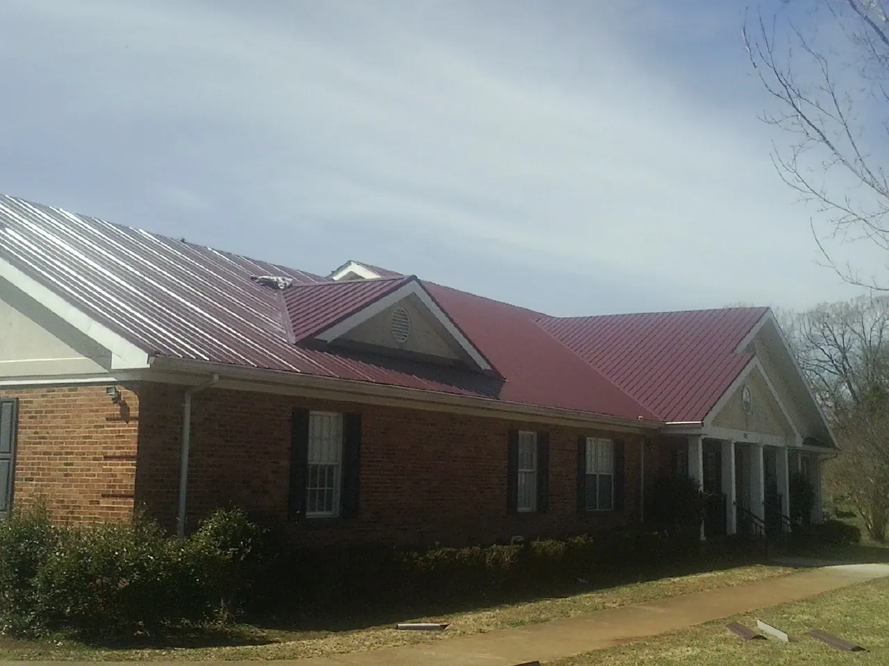 Red metal roof with gabled entries on a long brick building, from a Hail Damage Roof Repair job in Fort Deposit