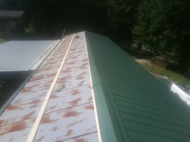 Old rusted panels beside newly installed green metal roofing — Wind Damage Roof Repair by Roofing Brothers in Fort Deposit