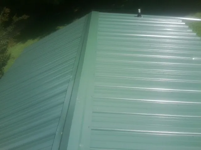 New green metal panels meeting at the ridge of a roof — Flat Roof Repair work by our crew in Fort Deposit