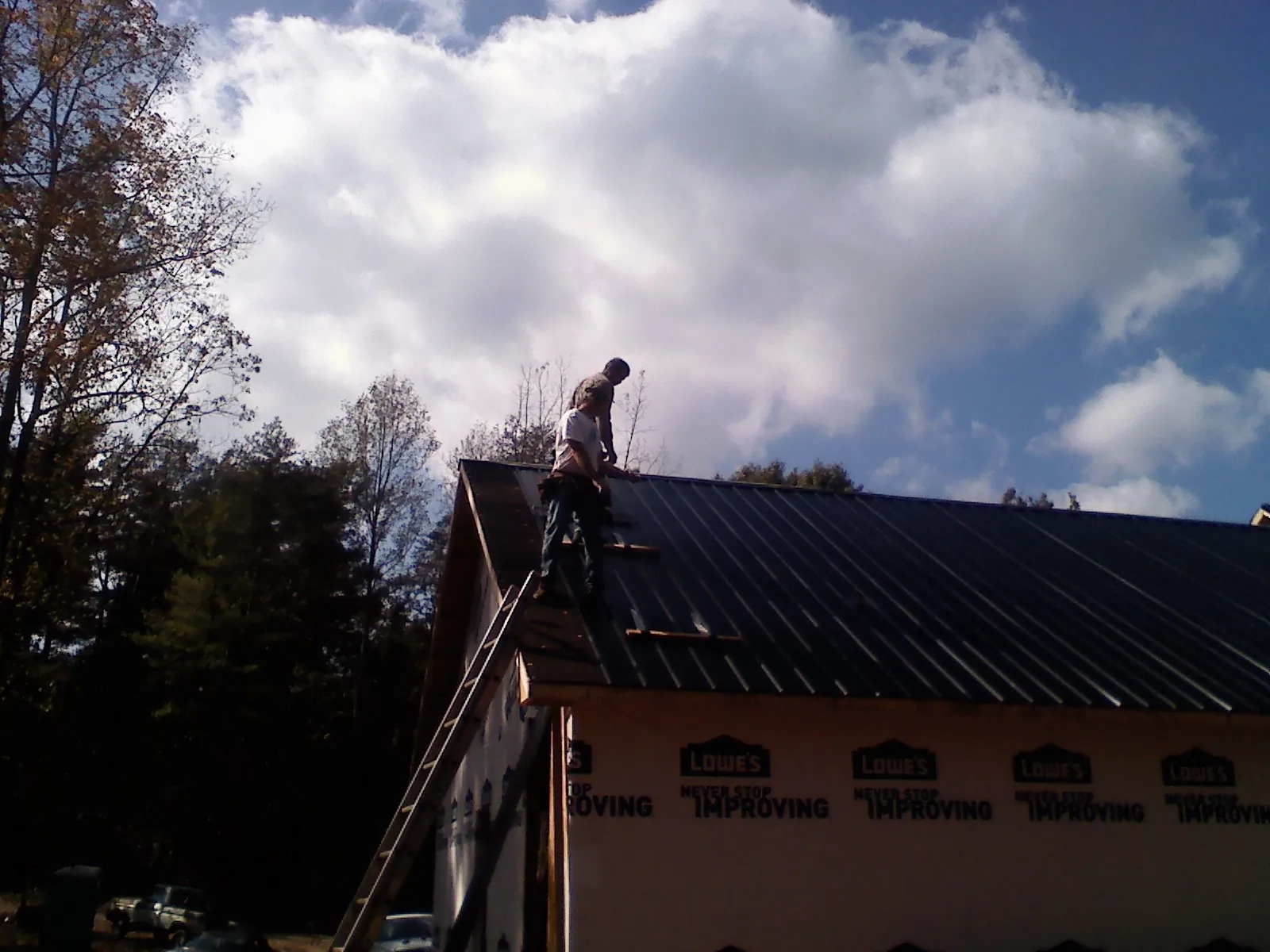 Roofer fastening dark metal panels high against a cloudy sky, from a Roof Inspection job in Fort Deposit