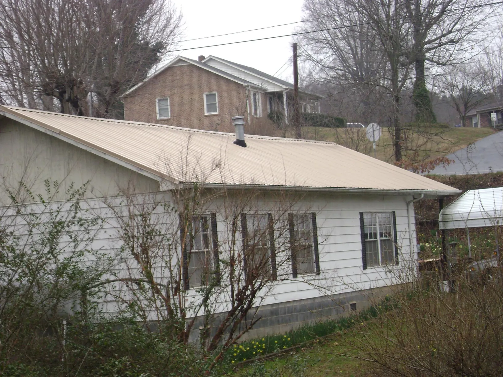 Tan metal roof on a white sided house set into a hillside — Commercial Roofing by Roofing Brothers in Fort Deposit