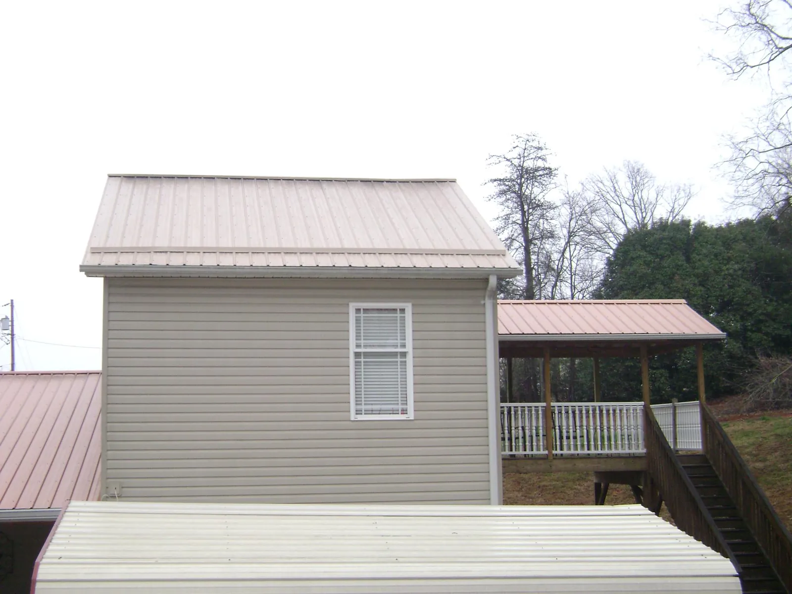 Tan metal roofs on a two story addition and attached porch, from a Roof Replacement job in Fort Deposit